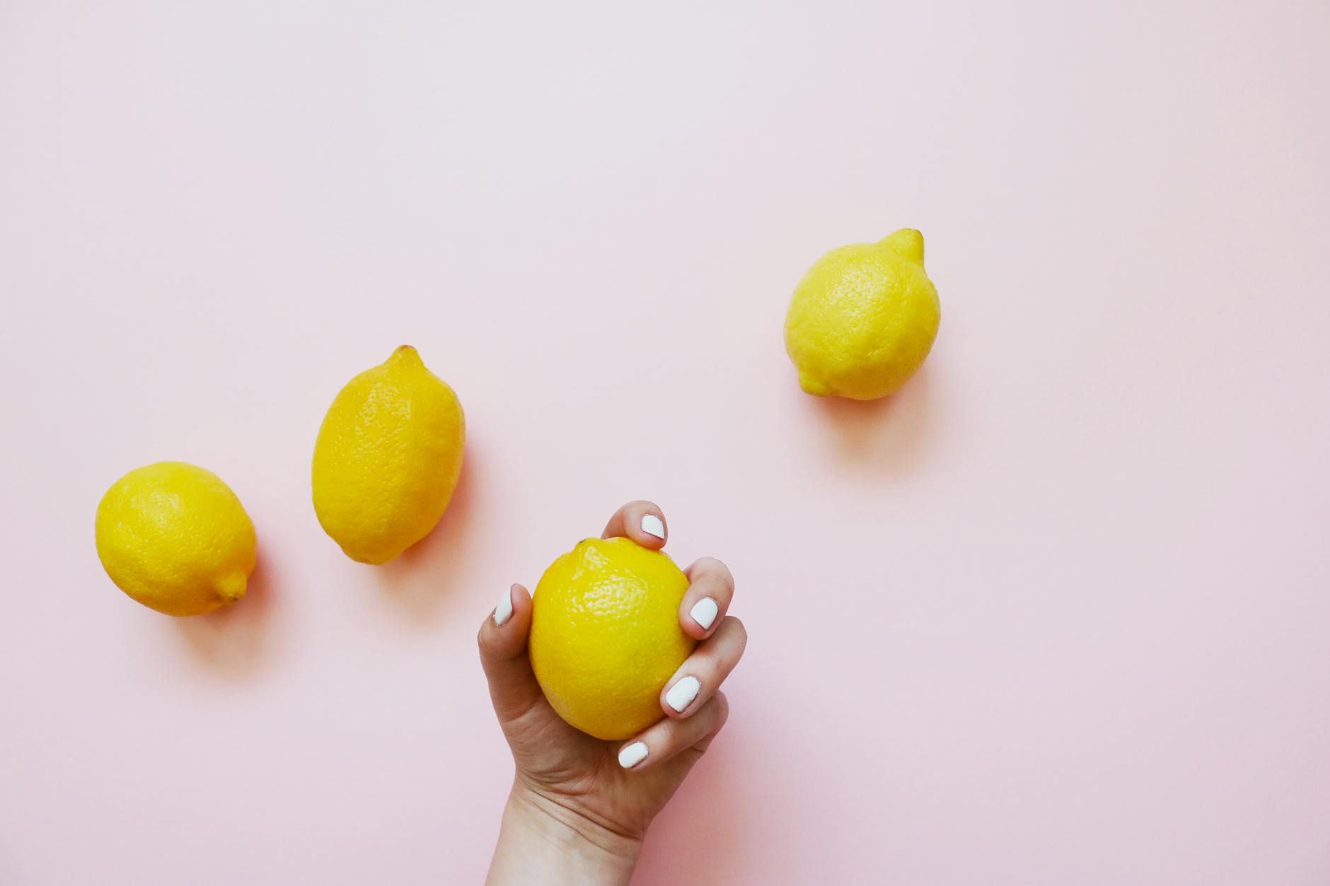 Hand holding a fresh lemon on a soft pink background, symbolizing renewal and sensation