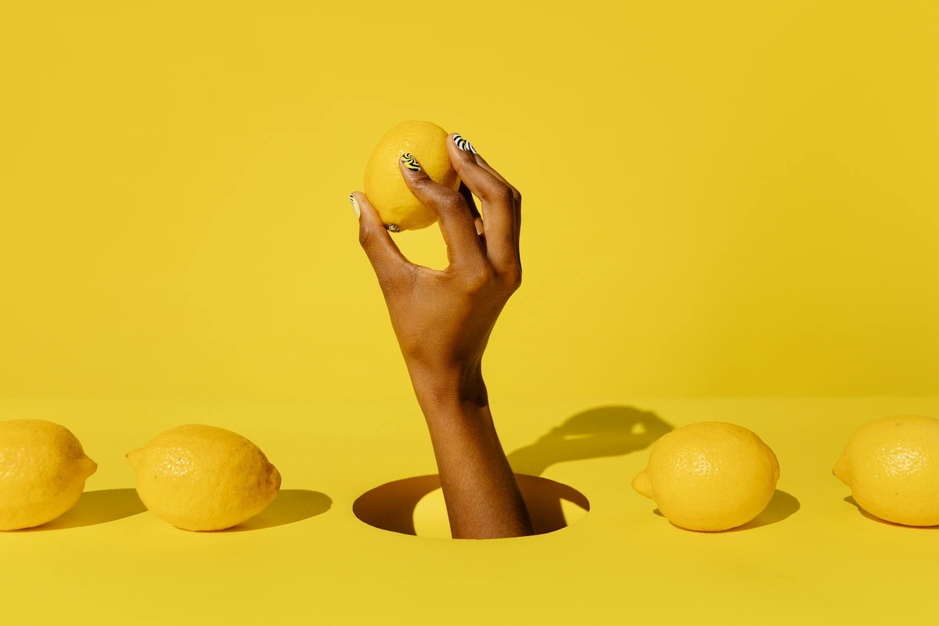A hand holding a fresh lemon against a bright yellow background, symbolizing renewed vitality and connection