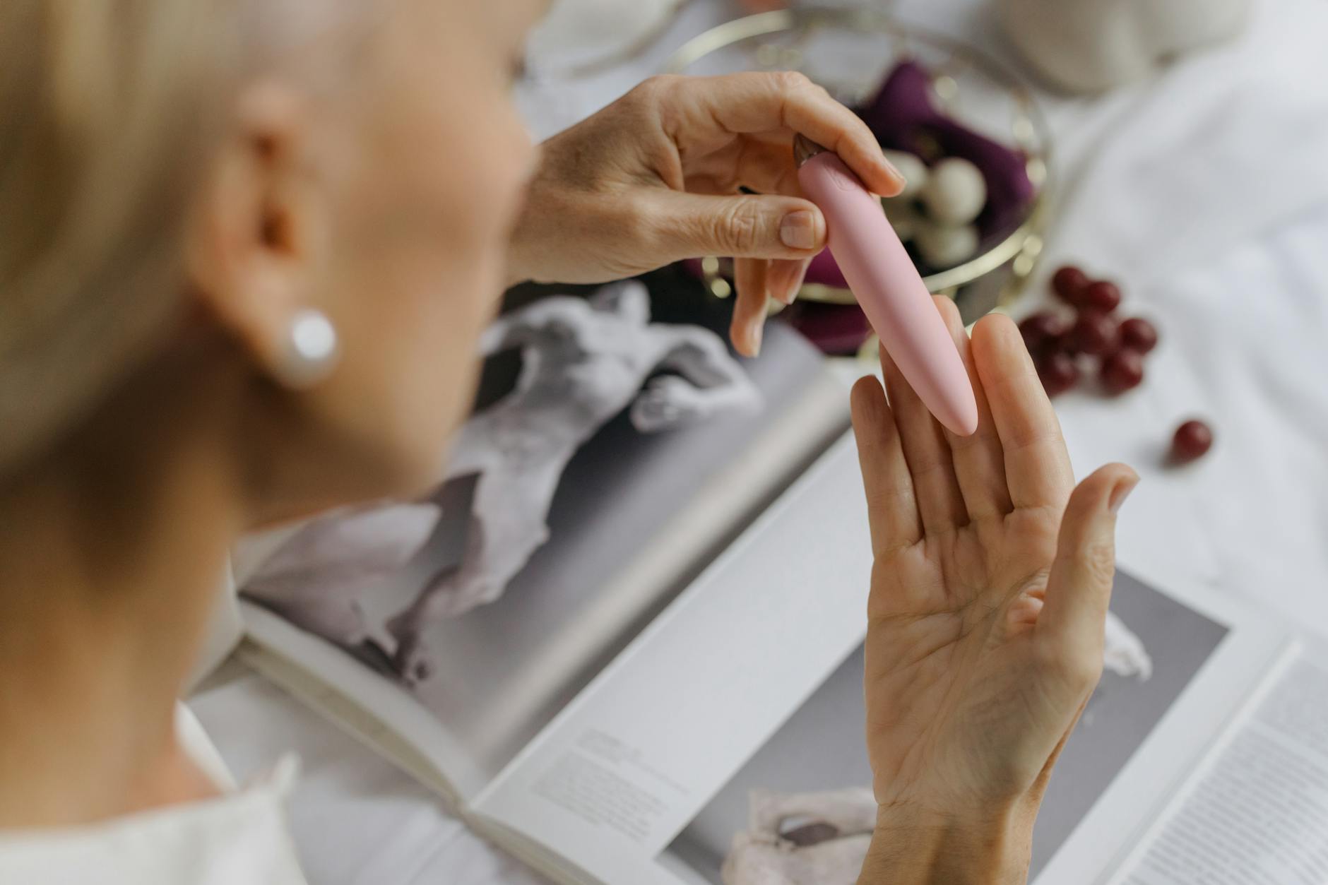 Close-up of hands holding a pink vibrator near books, illustrating intimate exploration with adult toys