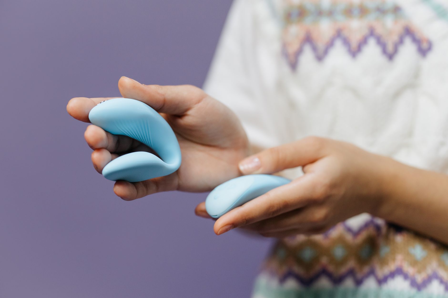 Hand holding a sleek blue clitoral vibrator against a purple background, symbolizing self-pleasure and body reclamation
