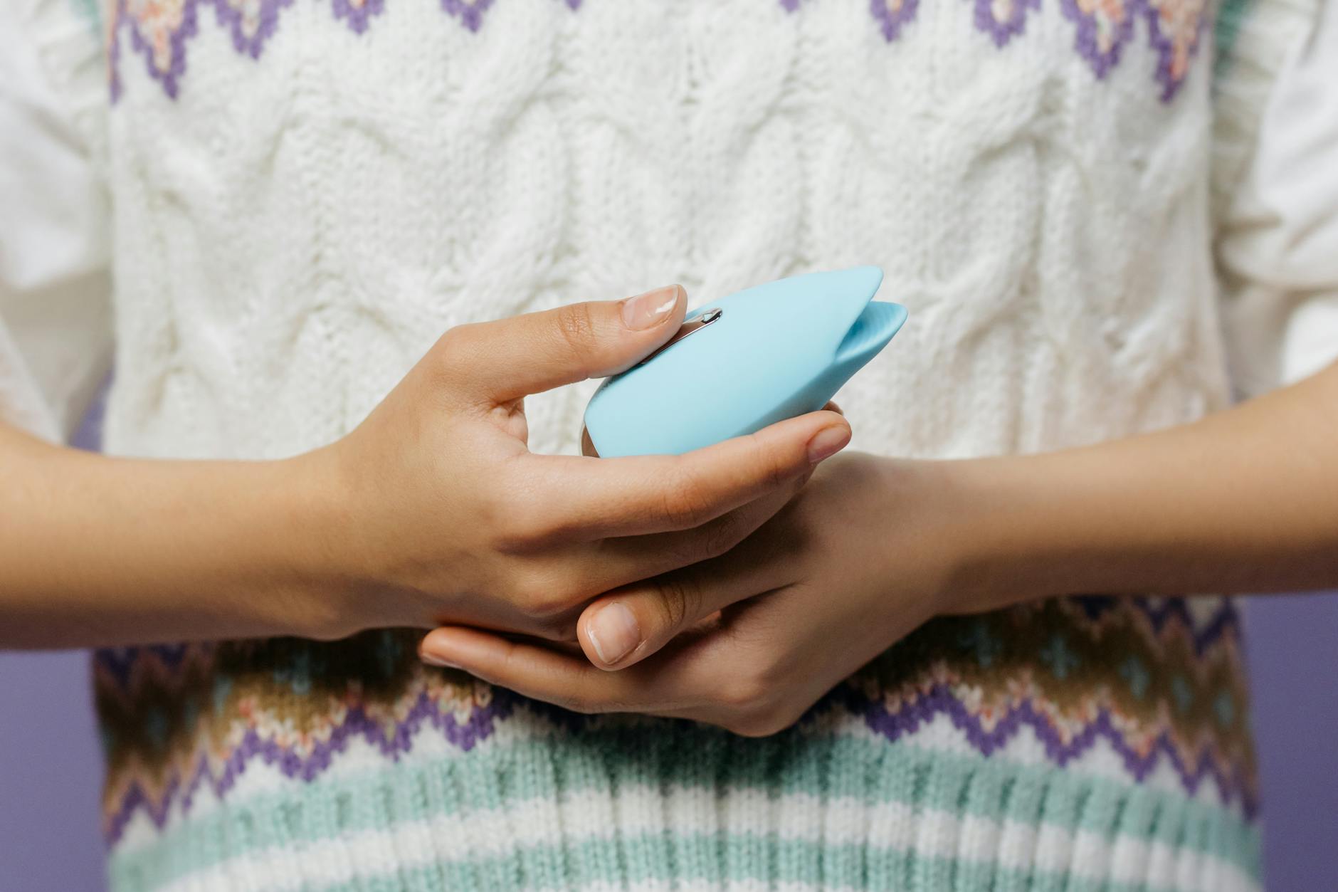 Close-up of hands holding a blue personal massager against a knitted sweater, representing safe reconnection after conflict.